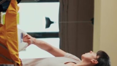 Vertical video: Angry woman throwing shirt at relaxed man, being frustrated about boyfriend not helping with housework. Stressed adult getting mad at life partner, doing spring cleaning at home