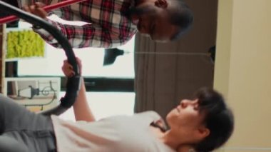 Vertical video: Diverse life partners dancing and singing with appliances, using mop and vacuum cleaner to wash apartment floors. Young couple having fun with music while they clean household