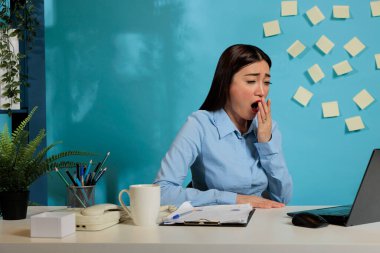 Female corporate employee trying to stay awake at work, exhausted from working overtime in the office. Professional woman working on project and finishing paperwork late at night.