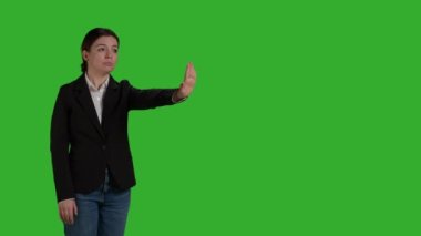 Side view of businesswoman showing no sign with palm, expressing negative gesture and denial in studio. Female worker in office suit doing rejection and refusal symbol over greenscreen.