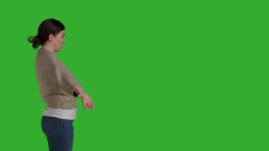 Profile of caucasian woman acting clueless and uncertain, doing i dont know gesture in studio. Young model expressing doubt and acting confused over greenscreen background, unsure person.