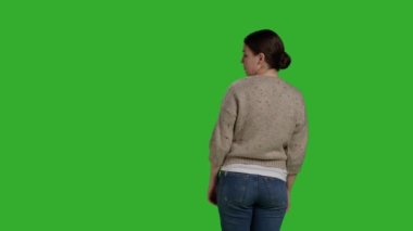 Back view of person showing denial and pushing something aside, expressing refusal and rejection looking displeased. Female model acting discontent and moving object, standing over greenscreen.