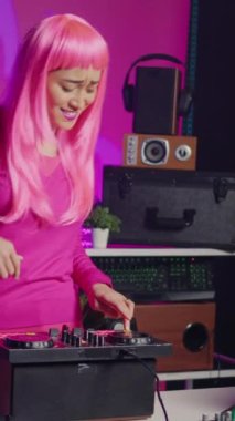 Vertical video: Dj performer having fun while playing electronic song at professional turntables, performing techno music in front of fans. Asian artist enjoying playing at nightclub using audio