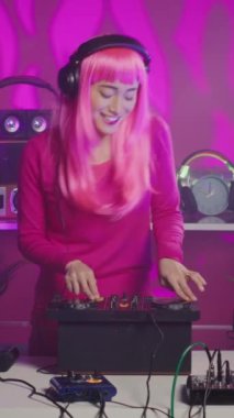 Vertical video: Musician with headset standing at dj table having fun while mixing stereo sounds with electronics. Cheerful performer enjoying to play music using professional mixer console in