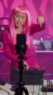 Vertical video: Artist performing song in studio recording mixing process with phone camera, playing eletronic song using professional turntables. Musician with pink hair having fun during performance