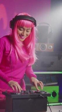 Vertical video: Asian performer playing electronic sound using mixer console, creating unique remix for fans during techno party in nightclub. Musician enjoying performing music using professional