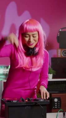 Vertical video: Artist recording mixing process with phone camera, performing eletronic music in night club using professional mixer console. Dj woman with pink hair having fun while performing techno