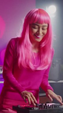 Vertical video: Dj artist using professional mixer console in nightclub, mixing techno sound creating unique remix for fans. Asian performer with pink hair playing musical album, performing eletronic