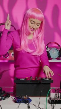 Vertical video: Artist with pink hair dancing and having fun in nightclub, mixing eletronic sound with techno using professional mixer. Dj performer playing remix using audio equipment, performing at