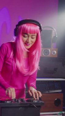 Vertical video: Artist standing at dj table mixing sound using mixer console, playing techno remix for fans during eletronic concert. Asian musician performing new album, enjoying having fun in club
