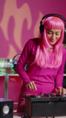Vertical video: Smiling musician working as dj playing song at mixer console, mixing techno music with eletronic using audio equipment. Performer with pink hair having fun in performing in club at