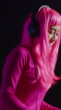 Vertical video: Cheerful artist working as dj playing song at turntables, mixing techno music with eletronic using audio equipment. Musician with pink hair having fun in performing in club at night