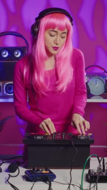 垂直ビデオ ピンク色の髪をしたミュージシャンは Djミキサーコンソールを使用してテクノ音楽を演奏し 夜のパーティーで楽しんでファンと曲を再生するのを楽しんでいます プロのオーディオでパフォーマンスを行うアーティスト — ストック動画