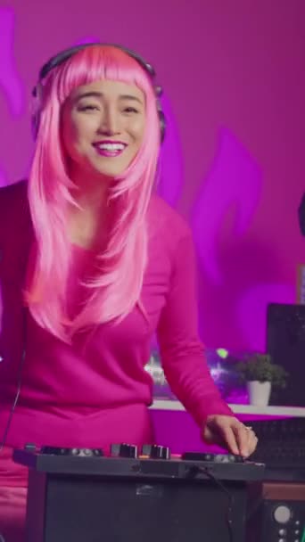 垂直ビデオ Djテーブルに立っているミュージシャンは プロのターンテーブルを使用して電子曲を演奏し クラブで夜の間に音楽を楽しむ ピンクの髪を持つアーティストがパフォーマンスを行う — ストック動画