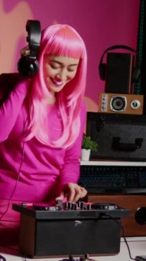 Vertical video: Musician using cutting-edge technology to remix music, listening song using headphones while performing in club at night time. Performer standing at dj table playing with professional