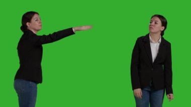 Close up of office manager raising arm and waving to call someone over, standing over isolated greenscreen backdrop. Young employee asking and calling people over to talk, businesswoman.