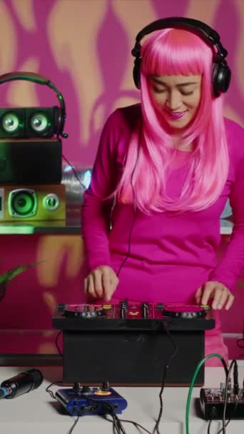 垂直视频 在夜总会的技术晚会上 Dj女人在开始使用音响设备混合音乐之前 会把耳机放在手机上 粉红头发的亚洲表演者与混音器一起创作音乐表演 — 图库视频影像