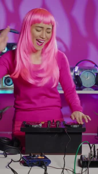 垂直ビデオ 陽気なパフォーマーは プロのミキサーコンソールでテクノリミックスを再生し 夜にクラブのファンと踊りや相互作用します オーディオを使用して電子サウンドを混合ピンクの髪を持つアーティスト — ストック動画