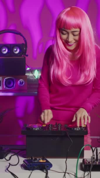 垂直ビデオ Djテーブルダンスでピンクの髪の立っているミュージシャンと電子機器とステレオサウンドを混合しながら 楽しみを持っています プロミキサーで音楽を演奏することを楽しむ笑顔のアーティスト — ストック動画