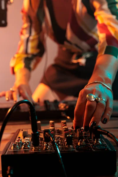 Female performer playing key sounds on mixing turntables, using audio dj equipment and stereo instrument to play techno music. Enjoying melody mix at nightclub, stage party in studio.