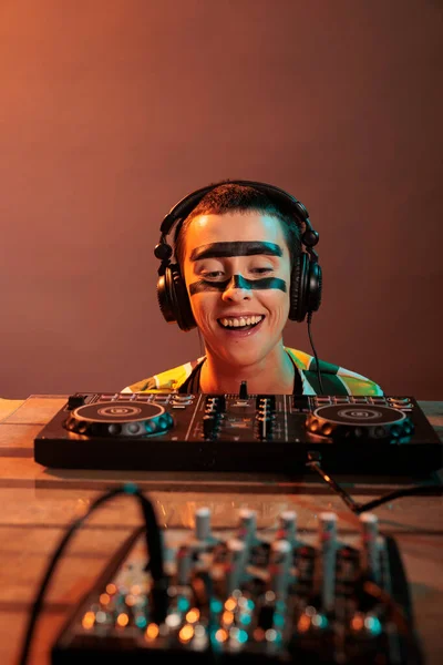 Young performer looking at dj turntables in studio, preparing to mix techno music and have fun at nightclub. Woman with crazy make up watching mixer on table, look closely and acting silly.
