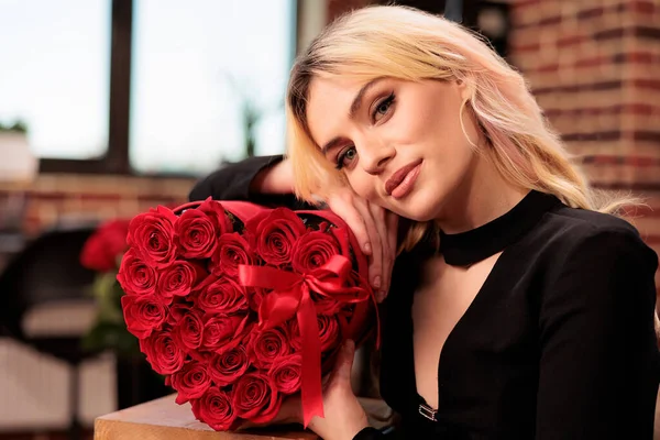 Φιλενάδα Στέκεται Στο Σαλόνι Γεμάτο Ρομαντικά Δώρα Κρατώντας Κόκκινα Τριαντάφυλλα — Φωτογραφία Αρχείου