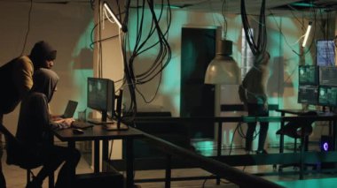 Dangerous spies using malware to hack network system, trying to steal data and passwords. Team of thieves committing hacktivism and identity theft, making threats at night. Tripod shot.