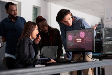 Team of software developers having web server hacked, reading critical error on computer display in agency. Multi ethnic programmers trying to solve hacking problem, firewall security.
