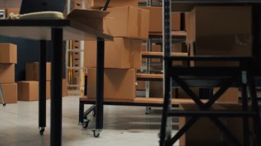 Storage room area filled with products packed in boxes, placed on shelves and racks in empty storehouse. Small business space used for shipping merchandise and doing stock inventory.