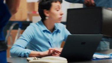 Business partners planning product shipment on laptop, shipping package order after doing distribution quality control. Diverse people checking merchandise stock and packaging. Handheld shot.