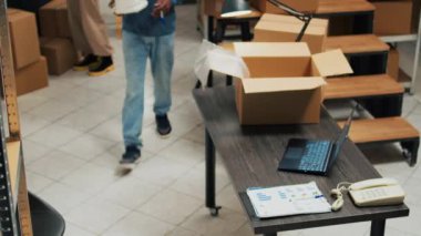 African american man putting products in cardboard boxes, preparing order for shipment. Young person doing quality control to ship merchandise to customers from storage room space.