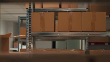 Storage room filled with cardboard boxes on shelves and racks, empty warehouse used to ship merchandise order to clients. Storehouse space with products, distribution work. Handheld shot.