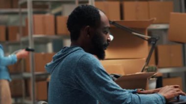 Male entrepreneur analyzing stock products and orders, doing inventory on laptop at warehouse. Young man using logistics and financial planning to send merchandise for development. Handheld shot.