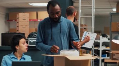 African american man signing delivery papers and shipping goods, working on packing warehouse merchandise. Small business owners doing product management with logistics. Handheld shot.