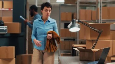 Female entrepreneur preparing order shipment fom storehouse, putting suppliees in cardboard boxes. Taking merchandise from storage shelves, working on distribution and logistics. Handheld shot.
