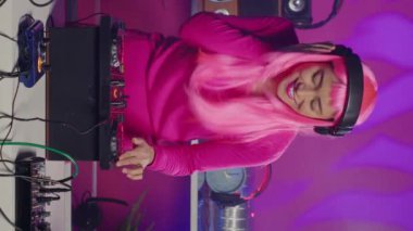 Vertical video: Asian performer mixing and mastering techno sound using professional turntables, enjoying performing music during night party in club. Dj artist doing performance with audio equipment