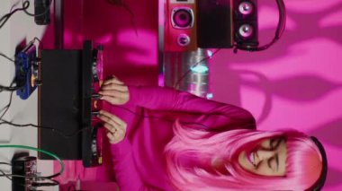 Vertical video: Smiling performer dancing and mixing techno sound with electronic using professional turntables, having fun during concert in nightclub. Performer standing over pink background in