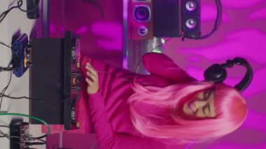 Vertical video: Smiling artist working as dj in night club mixing sounds at professional mixer console, enjoying dancing and performing for fans. Performer creating musical performance with techno