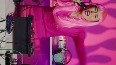 Vertical video: Smiling performer dancing and singing in nightclub, mixing eletronic sound with techno using professional mixer. Dj artist playing remix using audio equipment, performing at festival