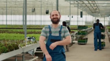 Kolları çaprazlanmış gülümseyen bir adamın portresi serada çeşitli işçilerle duruyor ve taze marul kasaları itiyor. Organik tarım işçisi biyo-sebzelerle mutlu görünüyor..
