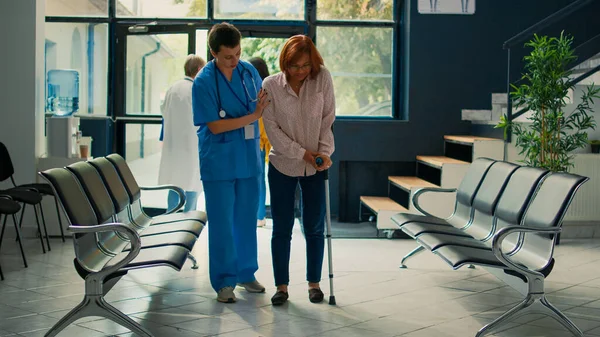 Hemşire, sakatlığı olan hastaya destek veriyor bastonla yürümeye çalışıyor, bacak kırığından sonra iyileşmek için yürüyüş yardımı kullanıyor. Fiziksel durumu ve fizyoterapiyi tedavi eden uzman biri..