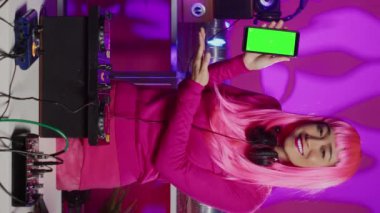 Vertical video: Cheerful artist presenting green screen mock up smartphone with isolated display, performing techno music in night club using professional mixer console. Dj performer enjoying to