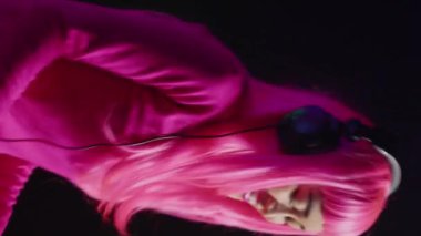 Vertical video: Cheerful artist working as dj playing song at turntables, mixing techno music with eletronic using audio equipment. Musician with pink hair having fun in performing in club at night