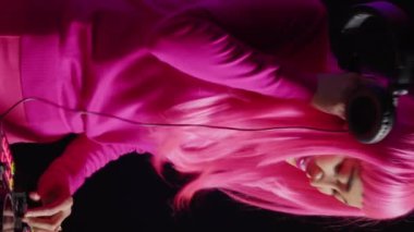 Vertical video: Musician having fun during performance talking with fans, mixing and mastering electronic sound using professional mixer console. Dj artist with pink hair performing music in club at
