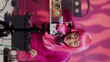 Vertical video: Dj performing electronic song at mixer filming process with mobile phone camera, talking with remote fans in studio. Musician mixing and mastering electronic sound using professional