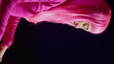 Vertical video: Musician with pink hair mixing and mastering techno sound using professional mixer console, performing music in nightclub. Performer playing electronic song, having fun during