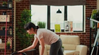 Casual girl using vacuum cleaner to tidy up apartment, cleaning dust and debris in living room. Young adult doing spring cleaning weekend activity chores, vacuuming wooden floors.