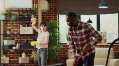 Young man washing dust and dirt off of living room floors, helping housewife with spring cleaning. Husband mopping tiles and sweeping grime, doing chores and housework together.