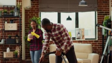 Young couple doing spring cleaning together in apartment space, focused people doing living room chores. Man vacuuming floors and woman sweeping dirt off of furniture, housework.