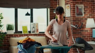 Aggressive wife throwing blouse at husband, being frustrated while she irons clothes at home. Modern woman being depressed and trying to clean household, doing spring cleaning chores.